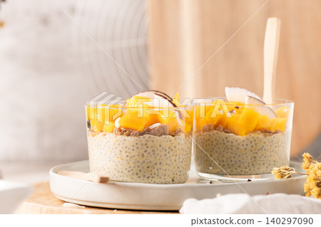 Healthy mango chia seed pudding in glass jars topped with fresh fruit chunks and coconut flakes served on a white plate with a wooden spoon for a nutritious breakfast or sweet summer snack Healthy mango chia seed pudding in glass jars topped with fresh fruit chunks and coconut flakes served on a white plate with a wooden spoon for a nutritious breakfast or sweet summer snack 140297090