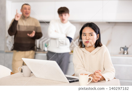 Disgruntled young woman trying to work on laptop while her husband and father scold and shout at her Disgruntled young woman trying to work on laptop while her husband and father scold and shout at her 140297182