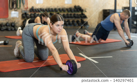 Sporty girl performing wheel rollout from knees in gym Sporty girl performing wheel rollout from knees in gym 140297401