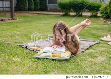 Girl lying on grass reading book in yard Girl lying on grass reading book in yard 140297403
