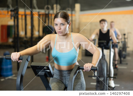 Concentrated young girl working out on stationary bicycle in gym Concentrated young girl working out on stationary bicycle in gym 140297408