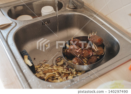 Peeling raw potatoes in a kitchen sink Peeling raw potatoes in a kitchen sink 140297490