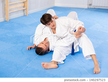 Two males practicing judo together on sports mats under the guidance of trainer Two males practicing judo together on sports mats under the guidance of trainer 140297523