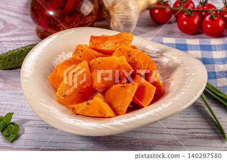 Roasted pumpkin cubes with herbs in white bowl surrounded by fresh vegetables on rustic wooden table Roasted pumpkin cubes with herbs in white bowl surrounded by fresh vegetables on rustic wooden table 140297580