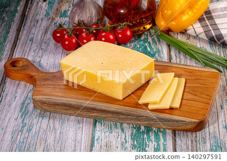 Sliced cheese on wooden board with fresh cherry tomatoes, garlic and pepper on rustic table 140297591