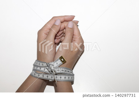Measuring tape restraining hands as symbol of eating disorder 140297731