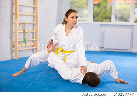 Young woman wearing kimono applying arm twist technique against middle-aged man Young woman wearing kimono applying arm twist technique against middle-aged man 140297777