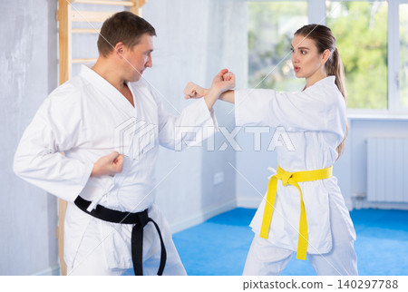 Young girl and middle-aged man practicing kicks and blocks in pair during karate courses Young girl and middle-aged man practicing kicks and blocks in pair during karate courses 140297788