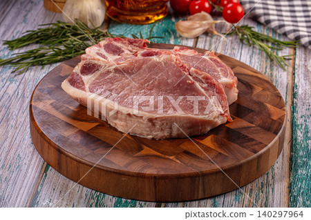 Raw pork chops on wooden cutting board with fresh rosemary, garlic, and tomatoes Raw pork chops on wooden cutting board with fresh rosemary, garlic, and tomatoes 140297964