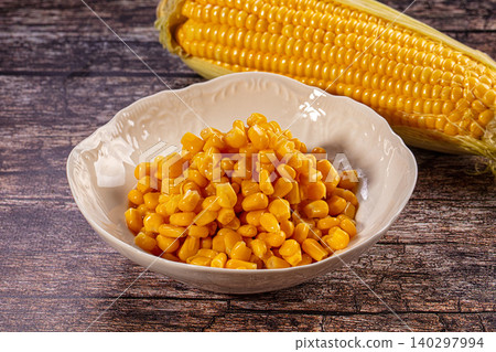 Fresh yellow corn kernels in white bowl with whole ear on wooden table Fresh yellow corn kernels in white bowl with whole ear on wooden table 140297994