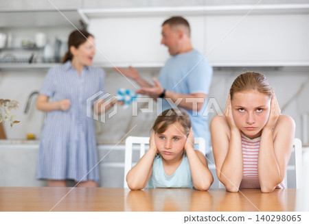 Upset teenage girls sitting in kitchen while parents quarreling Upset teenage girls sitting in kitchen while parents quarreling 140298065
