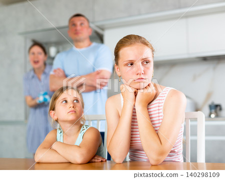 Frightened and frowning children sit at kitchen table during mom and dad quarrel 140298109