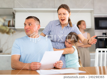 Angry woman chiding upset man sitting with papers in home kitchen Angry woman chiding upset man sitting with papers in home kitchen 140298365