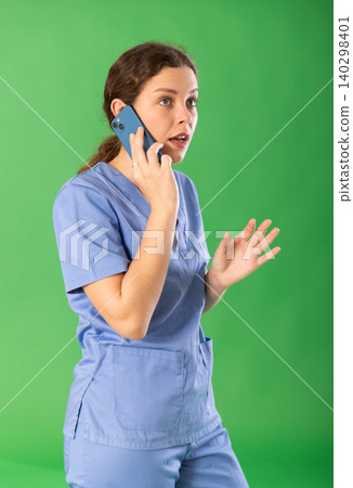 Young female nurse in blue uniform talking on smartphone Young female nurse in blue uniform talking on smartphone 140298401