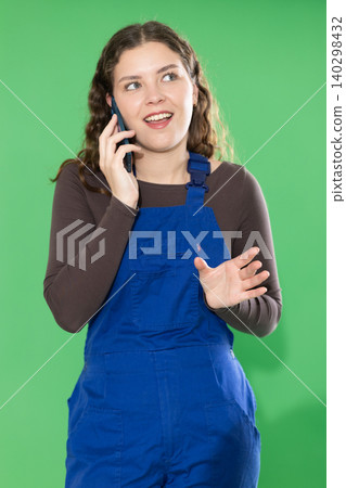 Female foreman in blue overalls is talking on mobile phone - placing an order for delivery of construction materials. Chroma key compositing Female foreman in blue overalls is talking on mobile phone - placing an order for delivery of construction materials. Chroma key compositing 140298432