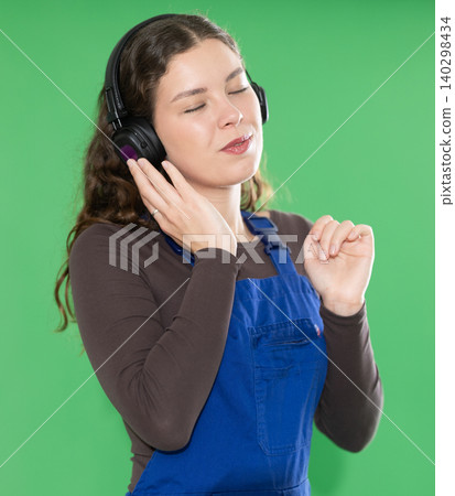 Young woman in blue overalls listening to music during break time Young woman in blue overalls listening to music during break time 140298434