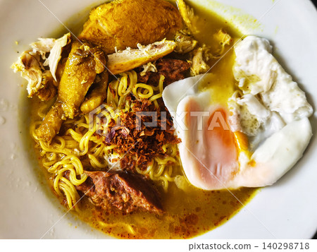 Close up of a bowl of hot Indonesian instant noodle soup with chicken, a soft-boiled egg, and crispy fried shallots. Close up of a bowl of hot Indonesian instant noodle soup with chicken, a soft-boiled egg, and crispy fried shallots. 140298718