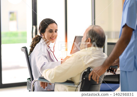 Old patient man sitting in wheelchair while young female doctor using stethoscope to check his heartbeat, elderly health checkup, happiness hospital. Old patient man sitting in wheelchair while young female doctor using stethoscope to check his heartbeat, elderly health checkup, happiness hospital. 140298831