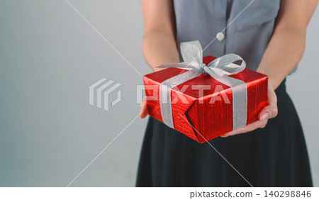 Red gift box with ribbon in hands woman for giving in holidays or celebration day with copy space for text. Holiday concept. Red gift box with ribbon in hands woman for giving in holidays or celebration day with copy space for text. Holiday concept. 140298846