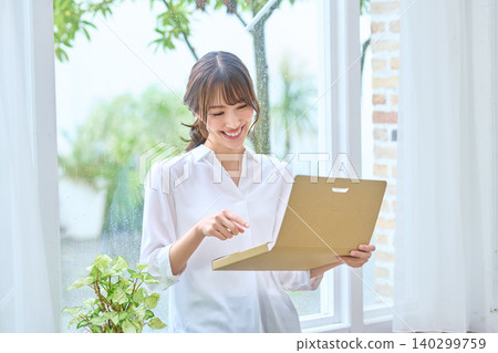 A smiling woman opening a package that arrived via mail order. A smiling woman opening a package that arrived via mail order. 140299759