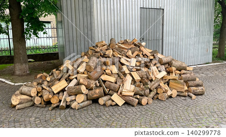 Large pile of chopped firewood on pavement near a metal building Large pile of chopped firewood on pavement near a metal building 140299778