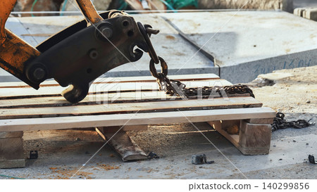 Excavator hook lifting wooden pallet with heavy chain on a construction site in Moscow 140299856