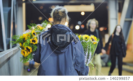 Woman carrying sunflowers on an urban pedestrian bridge at night, walking with gifts Woman carrying sunflowers on an urban pedestrian bridge at night, walking with gifts 140299857