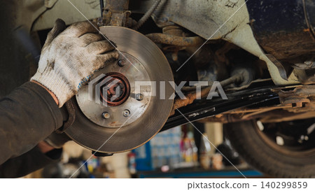 Mechanic replacing brake disc of a car using a wrench 140299859