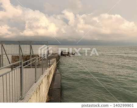 atmospheric coastal scene with concrete pier or jetty extending into the sea. A sense of impending weather over the tranquil waterfront. atmospheric coastal scene with concrete pier or jetty extending into the sea. A sense of impending weather over the tranquil waterfront. 140299901
