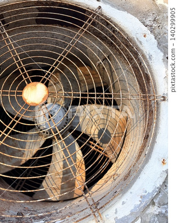 A fan behind a metal grille creates an industrial atmosphere. Large industrial exhaust fan with protective grille, front view A fan behind a metal grille creates an industrial atmosphere. Large industrial exhaust fan with protective grille, front view 140299905