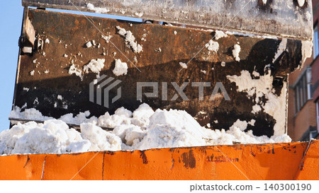 Snow removal equipment loading fresh snow into bright orange truck container 140300190