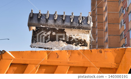 Excavator bucket loading snow into a dump truck, urban winter cleaning Excavator bucket loading snow into a dump truck, urban winter cleaning 140300191
