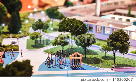 Miniature public park model with people enjoying playground and city lights at night 140300207