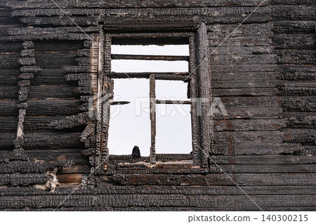 Burnt wooden wall with charred texture and ruined window frame after a devastating fire Burnt wooden wall with charred texture and ruined window frame after a devastating fire 140300215