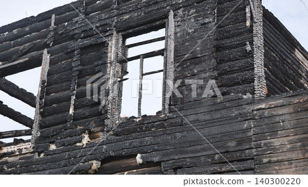 Exterior of a fire-damaged wooden house with charred black walls and an empty window frame Exterior of a fire-damaged wooden house with charred black walls and an empty window frame 140300220