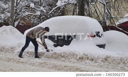 Man shoveling snow off car after heavy snowfall, facing winter challenge Man shoveling snow off car after heavy snowfall, facing winter challenge 140300273