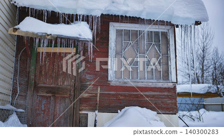 Rustic wooden house covered in snow and icicles during a harsh freezing winter Rustic wooden house covered in snow and icicles during a harsh freezing winter 140300283