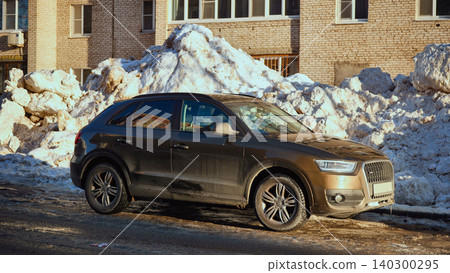 Muddy brown SUV parked in front of snow piles during harsh winter 140300295