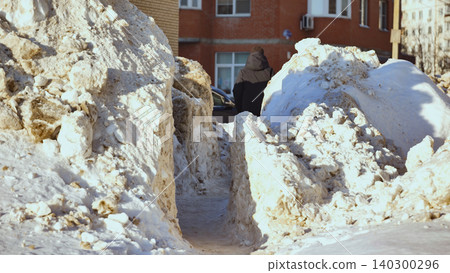 Person walking through narrow path between huge dirty snowdrifts in harsh winter city Person walking through narrow path between huge dirty snowdrifts in harsh winter city 140300296