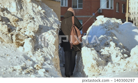 Woman walking through snowdrifts in winter city navigating urban environment Woman walking through snowdrifts in winter city navigating urban environment 140300297