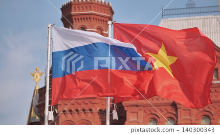 Flags of Russia and Vietnam waving together in front of a historic red brick building against a blue sky. Flags of Russia and Vietnam waving together in front of a historic red brick building against a blue sky. 140300343