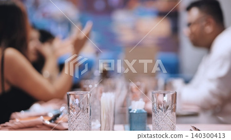 Dinner table setting with glassware and blurred people enjoying social gathering Dinner table setting with glassware and blurred people enjoying social gathering 140300413