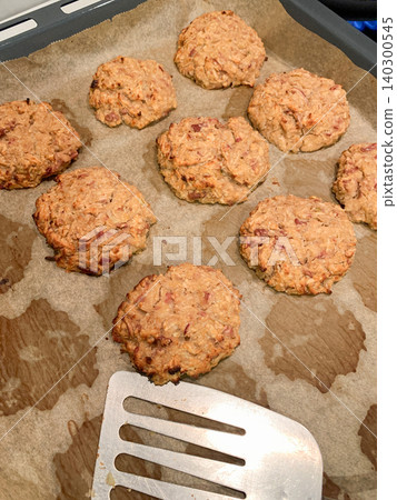 Pancakes made with carrot and apple are laid out on a baking tray. A spatula is placed beside them, showing they are ready to be served. The setting is a kitchen area Pancakes made with carrot and apple are laid out on a baking tray. A spatula is placed beside them, showing they are ready to be served. The setting is a kitchen area 140300545