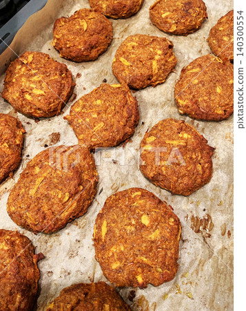 Pancakes made with carrot and apple are laid out on a baking tray. A spatula is placed beside them, showing they are ready to be served. The setting is a kitchen area 140300554