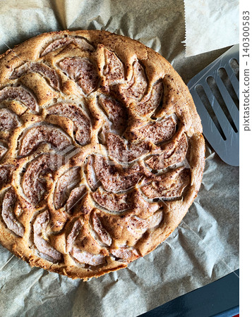 A gluten-free pear pie sits on a plate in a kitchen. The pie has slices of pear arranged on top. A fresh pear is beside the pie, creating a simple dessert scene in the afternoon light A gluten-free pear pie sits on a plate in a kitchen. The pie has slices of pear arranged on top. A fresh pear is beside the pie, creating a simple dessert scene in the afternoon light 140300583