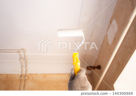 Man holding roller near freshly painted ceiling. Enjoyable weekend project. Cosmetic renovation done simply and affordably Man holding roller near freshly painted ceiling. Enjoyable weekend project. Cosmetic renovation done simply and affordably 140300989