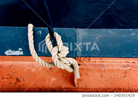 Close-up of mooring rope with knotted end tied around cleat on pier equipment Close-up of mooring rope with knotted end tied around cleat on pier equipment 140301429
