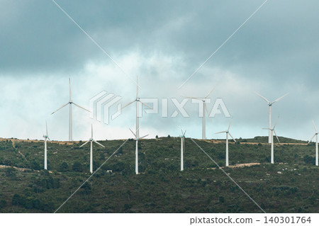 Wind turbines on a mountain ridge under dramatic storm clouds in Catalonia Spain, renewable energy infrastructure generating clean electricity 140301764