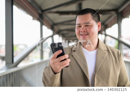 Plus size Isan Thai man smiling at his phone on a bridge walkway Plus size Isan Thai man smiling at his phone on a bridge walkway 140302125