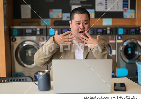 Surprised plus size Isan Thai man gesturing at laptop at a laundromat Surprised plus size Isan Thai man gesturing at laptop at a laundromat 140302165